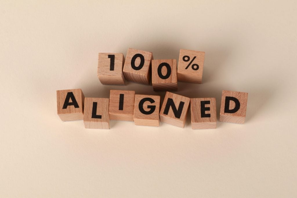 Wooden blocks spelling '100% Aligned' on a neutral background, conveying precision and alignment.