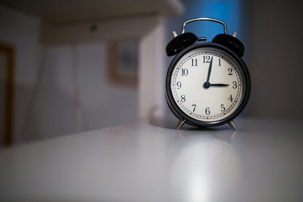 A classic black alarm clock with a white face showing 7:05, placed on a white surface.